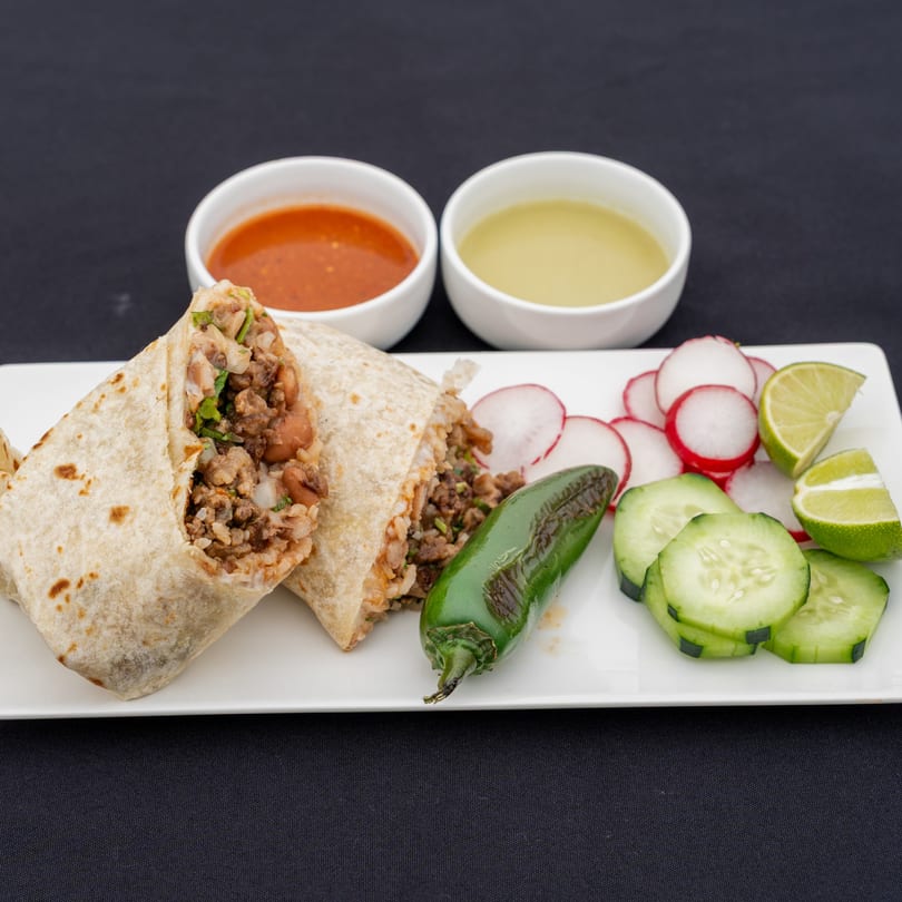 Two Blady's Tacos burritos with sides of salsa, radishes, cucumbers, lime, and a green chili.