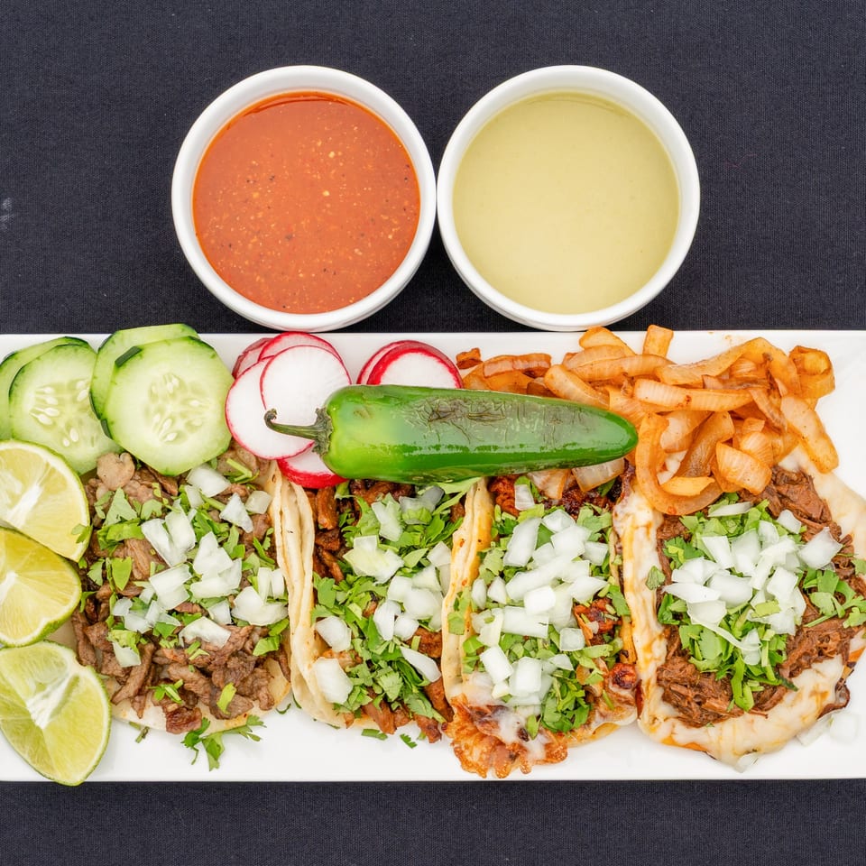 Four Blady's Tacos with various meats, cilantro, onions, limes, cucumbers, radishes, and sauces.